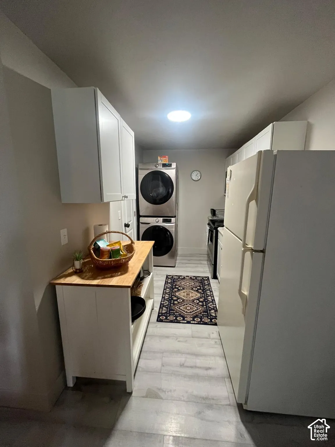 Galley-style kitchen with white cabinetry, light wood-finish flooring, and a stacked washer/dryer unit