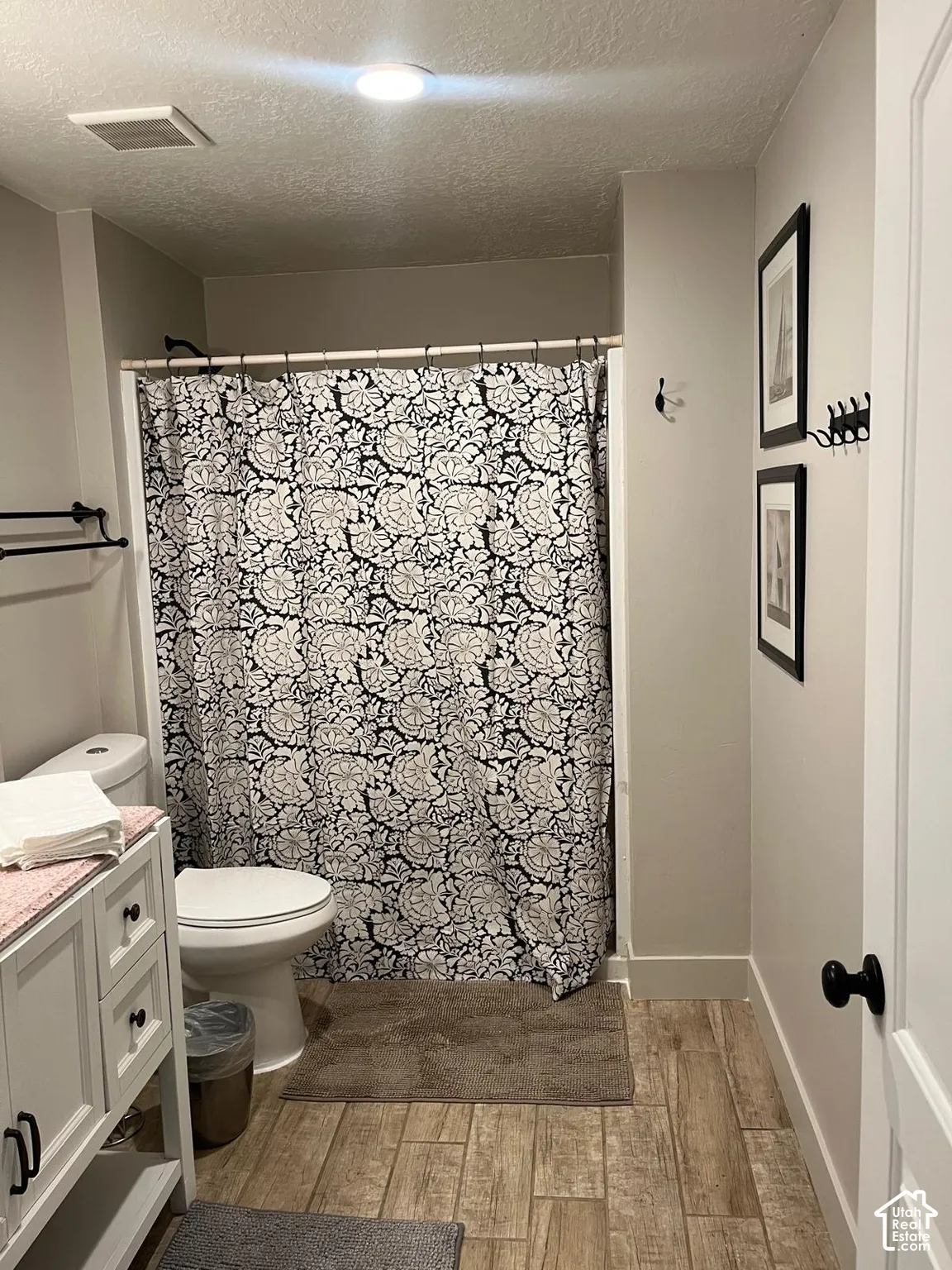 White vanity with black hardware, toilet, and a combination shower/tub with a black shower rod, set on wood-finish flooring