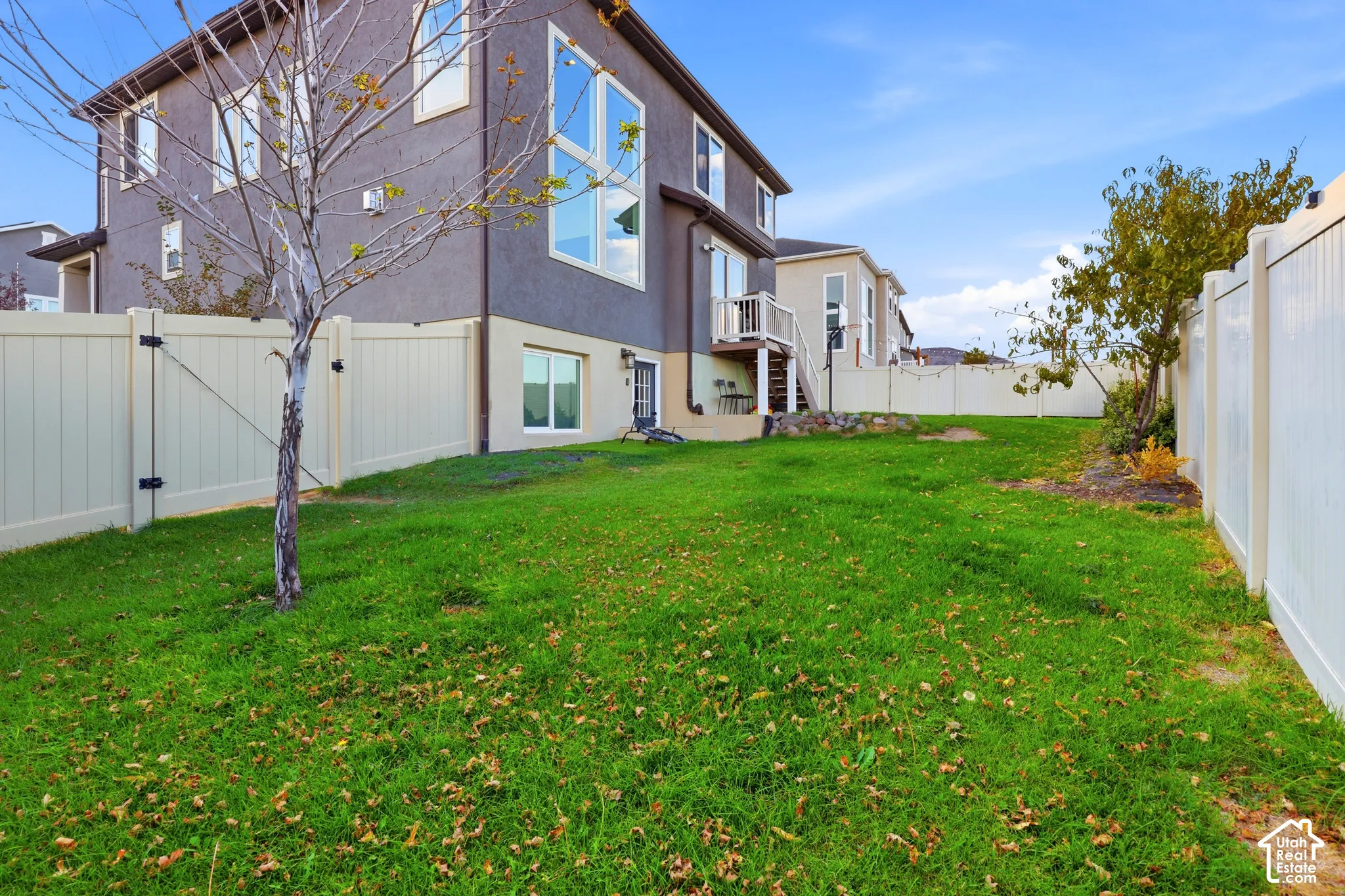 Spacious backyard with mature landscaping, manicured lawn, and white vinyl privacy fencing