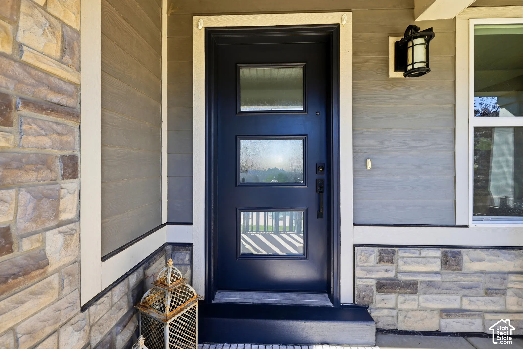 Entryway featuring a dark paneled door with three glass inserts, stone veneer, horizontal siding, and an exterior wall lantern