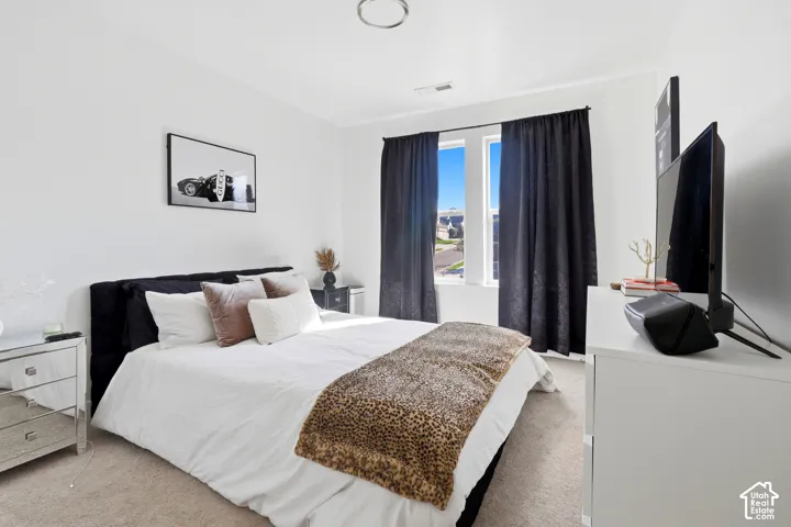 Carpeted bedroom featuring a dark upholstered headboard, white walls, and a ceiling-mounted light fixture