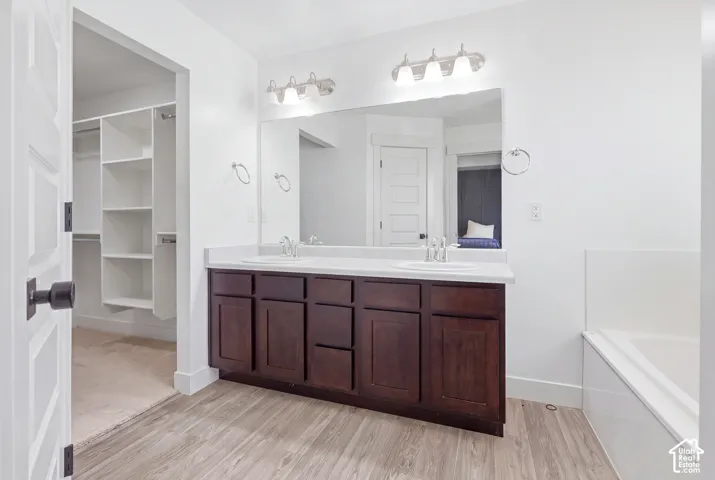 Dual vanity with wood-finish cabinetry and white countertops, large mirror, chrome light fixture, and wood-finish flooring