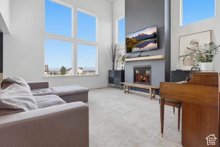 High ceilings with extensive window fenestration, a built-in fireplace with a wood mantle, and light-toned carpet flooring