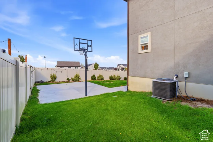 Expansive green lawn with a concrete patio area, vinyl fencing, and a stucco exterior