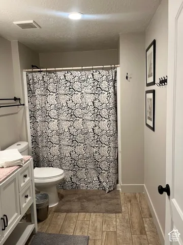 White vanity with black hardware, toilet, and a combination shower/tub with a black shower rod, set on wood-finish flooring