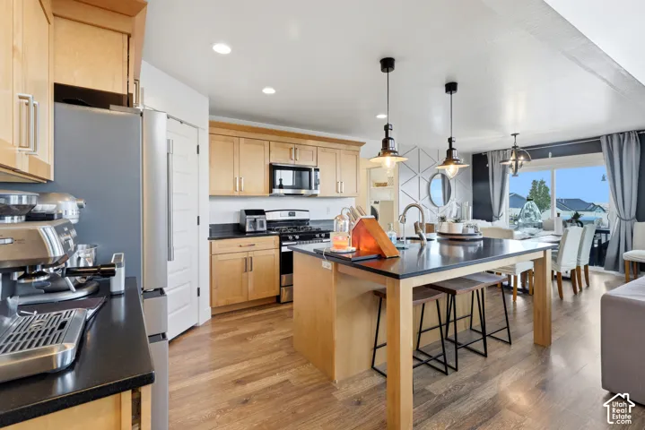 Kitchen featuring wood-finish flooring, recessed lighting, light wood cabinetry, dark countertops, and a kitchen island with pendant lighting