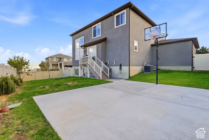 Expansive concrete patio with a basketball hoop, leading to a manicured lawn area
