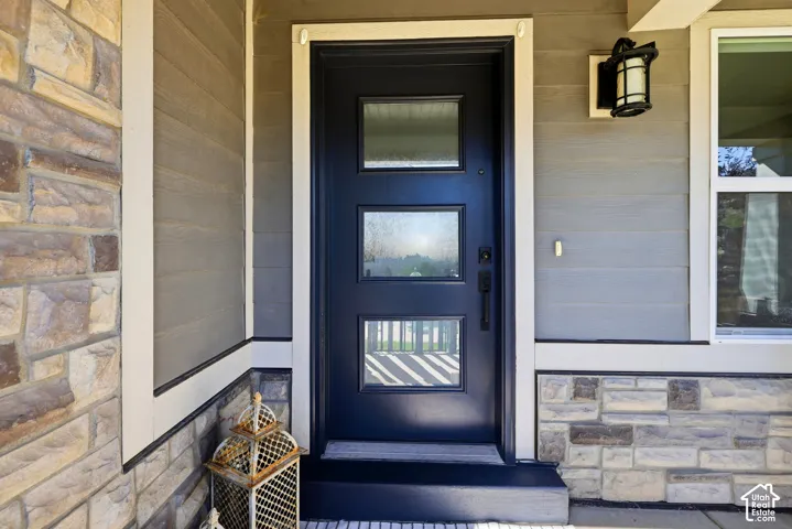 Entryway featuring a dark paneled door with three glass inserts, stone veneer, horizontal siding, and an exterior wall lantern