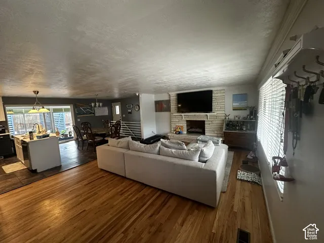 Hardwood flooring throughout, stone-clad fireplace, kitchen island with sink, pendant lighting, and large windows