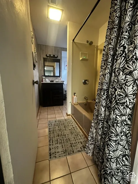 Ceramic tile flooring, vanity with dark wood-finish cabinetry, rectangular mirror, three-light vanity fixture, and a built-in bathtub with shower