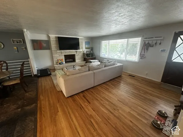 Wood-finish flooring, brick-faced fireplace with hearth, multiple windows, and a paneled entry door with decorative glass inserts