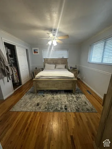 Hardwood flooring, crown molding, double windows with horizontal blinds, ceiling fan with integrated lighting, and a bi-fold closet with built-in shelving