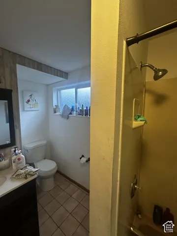 Bathroom featuring a vanity with a white countertop, a white toilet, tiled flooring, and a shower with a dark bronze shower rod and showerhead