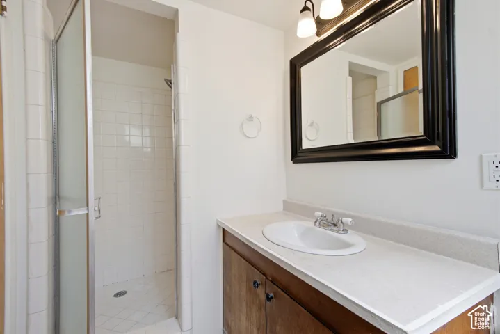 Vanity with an integrated sink, framed mirror, and a shower enclosure with white tile