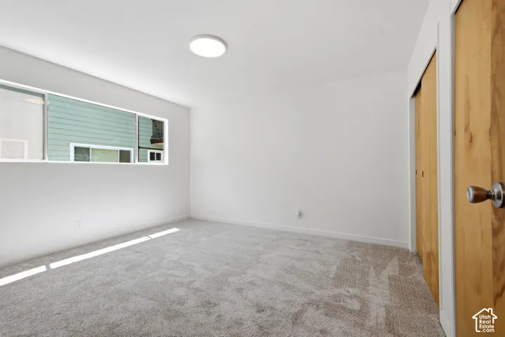Light-colored carpeting, horizontal window, ceiling-mounted light fixture, wood-finish sliding closet doors, and white walls