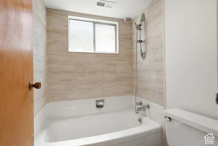 Bathtub with light-toned tiled surround, chrome shower fixture, and a sliding window