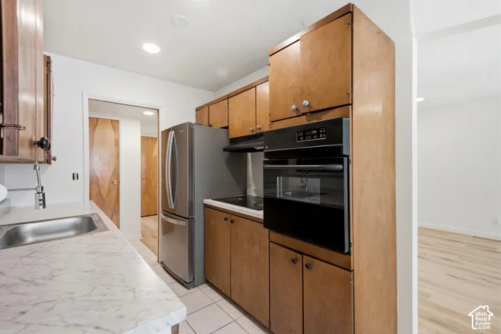 White marble-finish countertops, stainless steel refrigerator, built-in wall oven, wood cabinetry, and recessed lighting