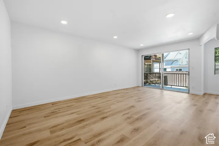 Spacious room with wood-finish flooring, recessed lighting, and a sliding glass door leading to a balcony with black railings