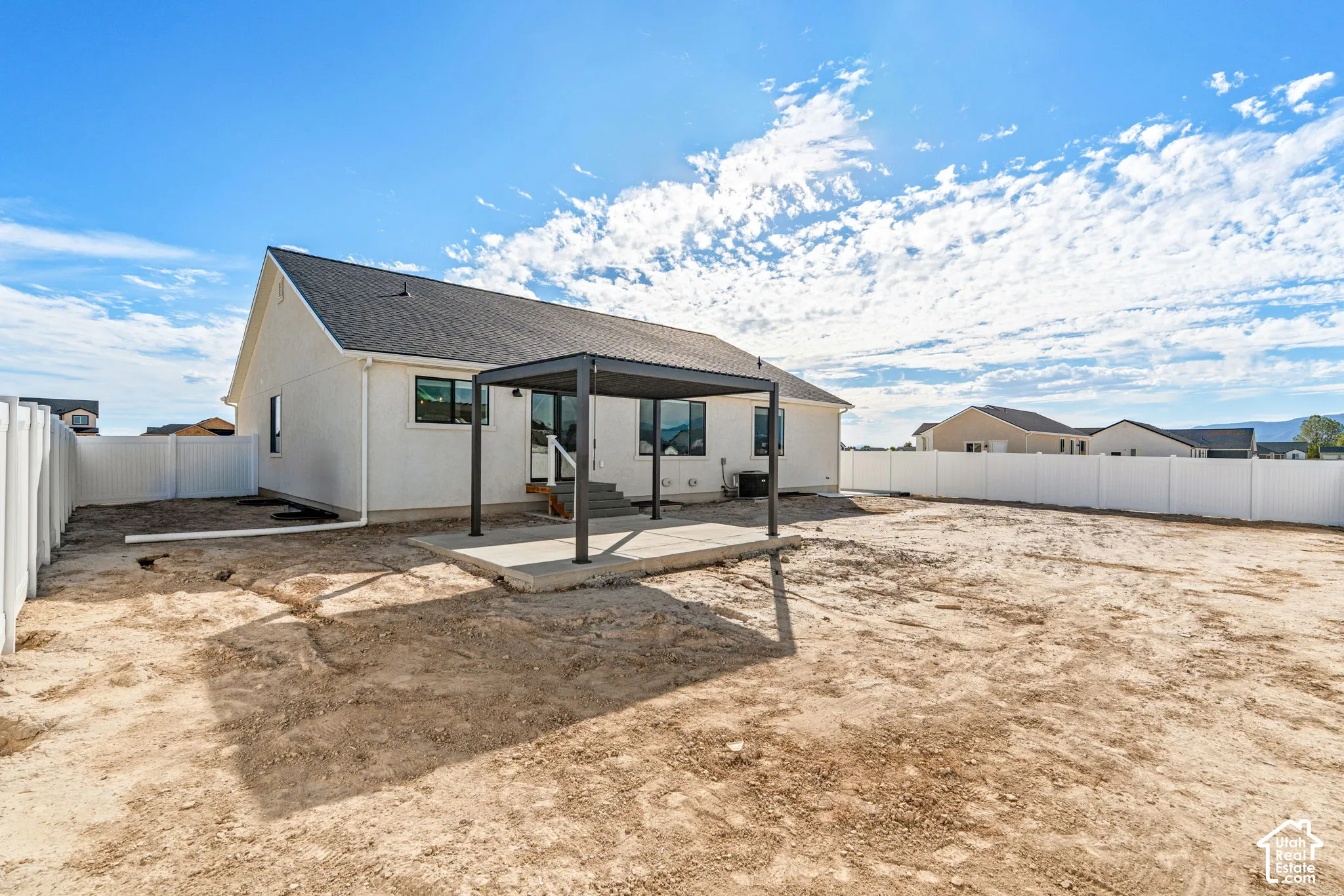 Rear exterior featuring a white vinyl privacy fence, dark gray pergola, concrete patio, and a sloped roofline