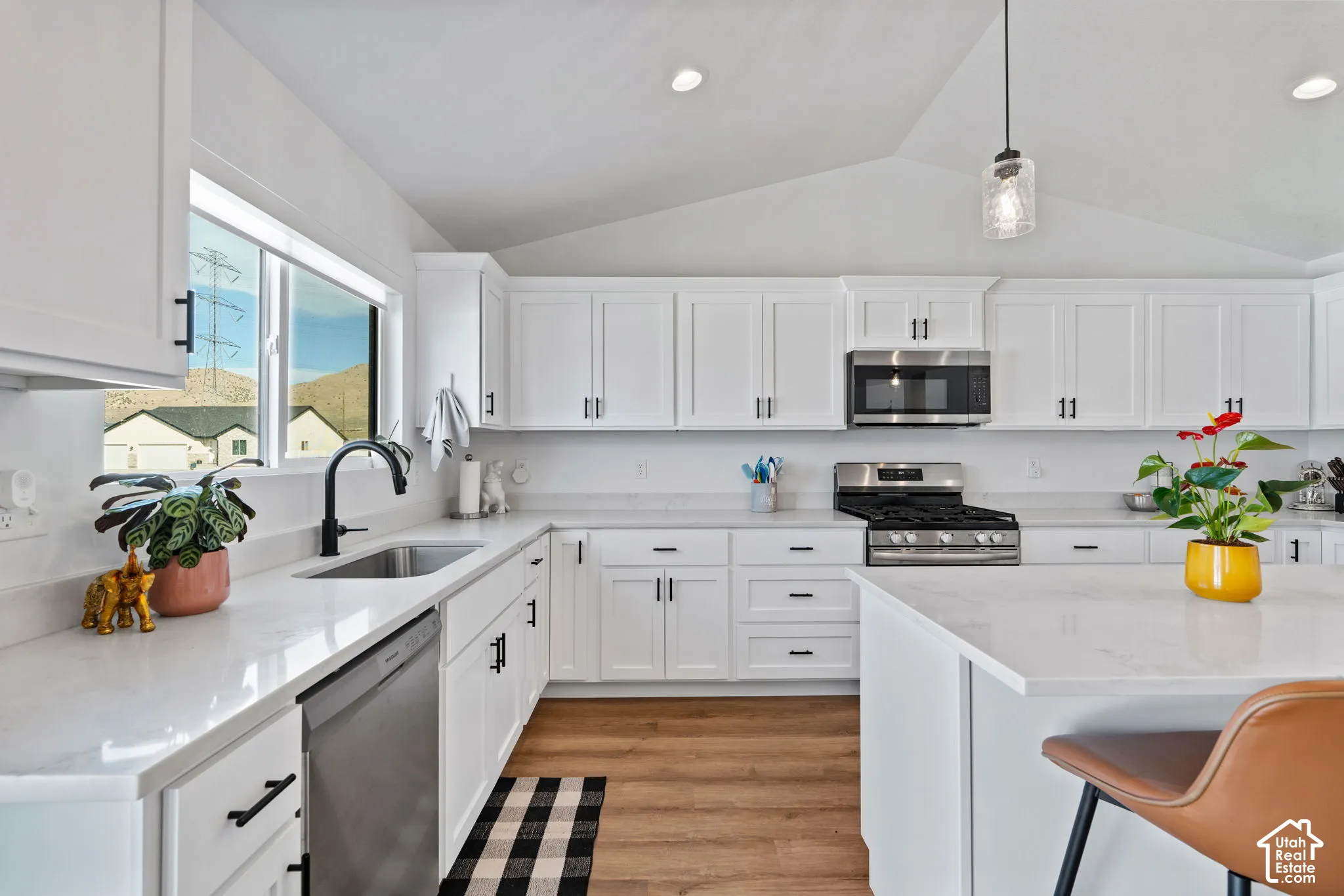 Vaulted ceiling with recessed lighting, white cabinetry with black hardware, stainless steel appliances, light-toned countertops, and wood-finish flooring