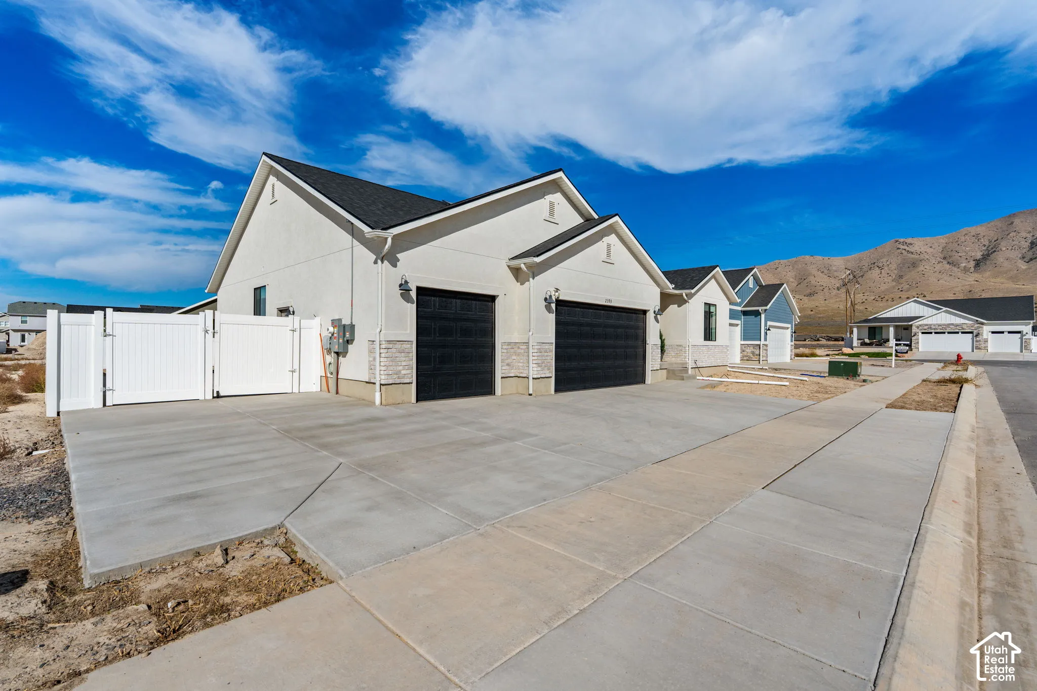 Stucco exterior with stone veneer accents, multi-car concrete driveway, black garage doors, and a white gate