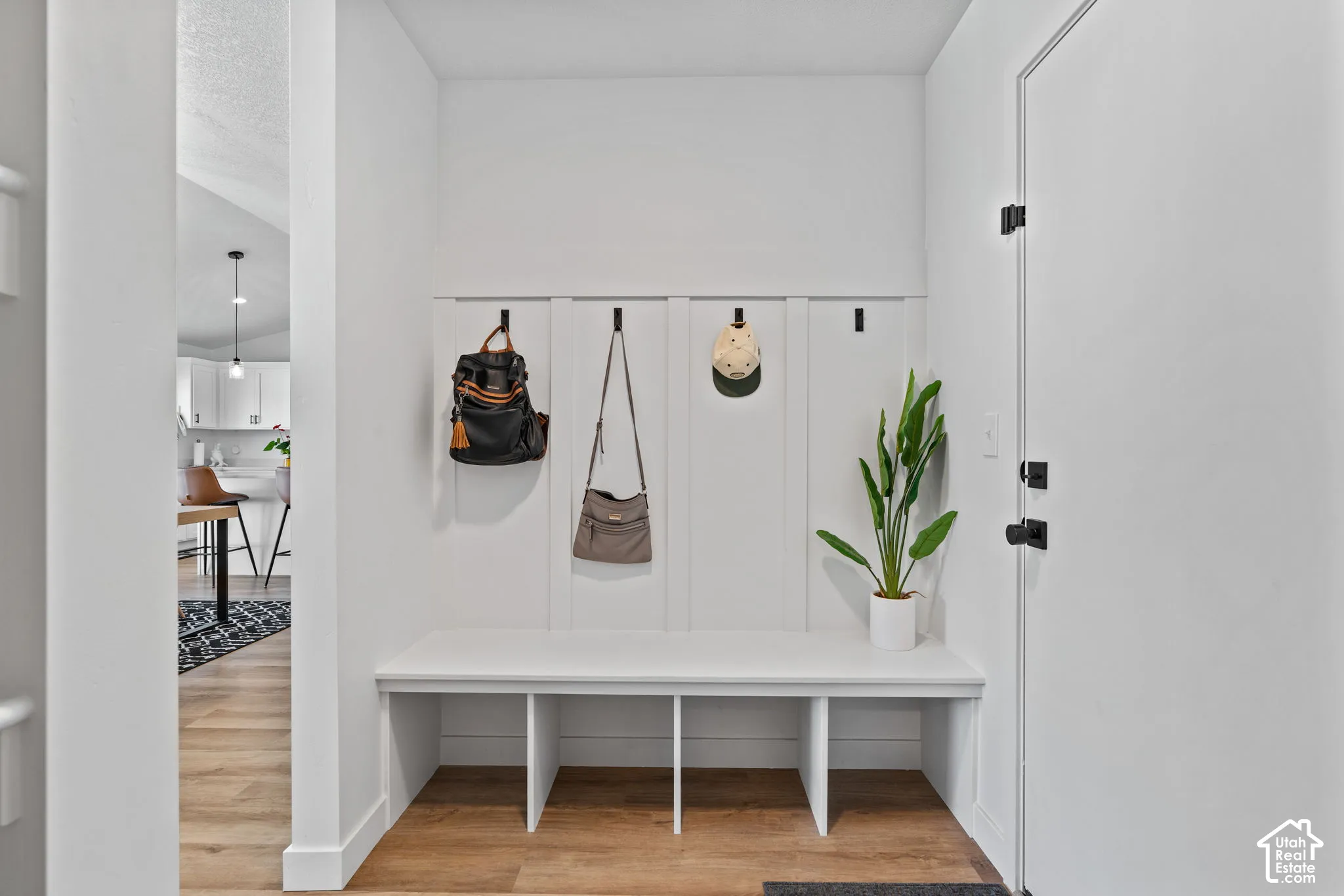 Built-in bench with storage, board and batten wall with hooks, wood-finish flooring, and a white entry door with matte black hardware