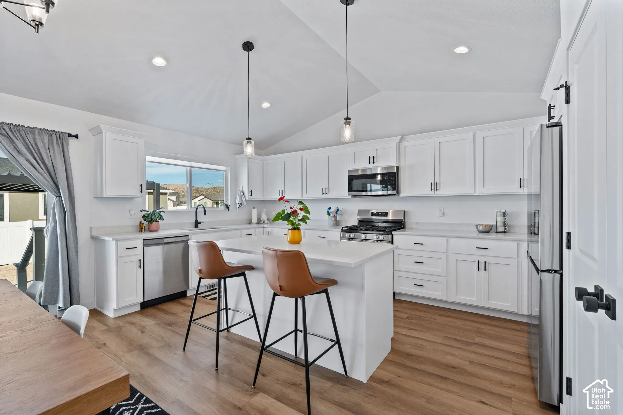 Kitchen featuring white shaker cabinetry, stainless steel appliances, a center island, wood-finish flooring, and vaulted ceilings