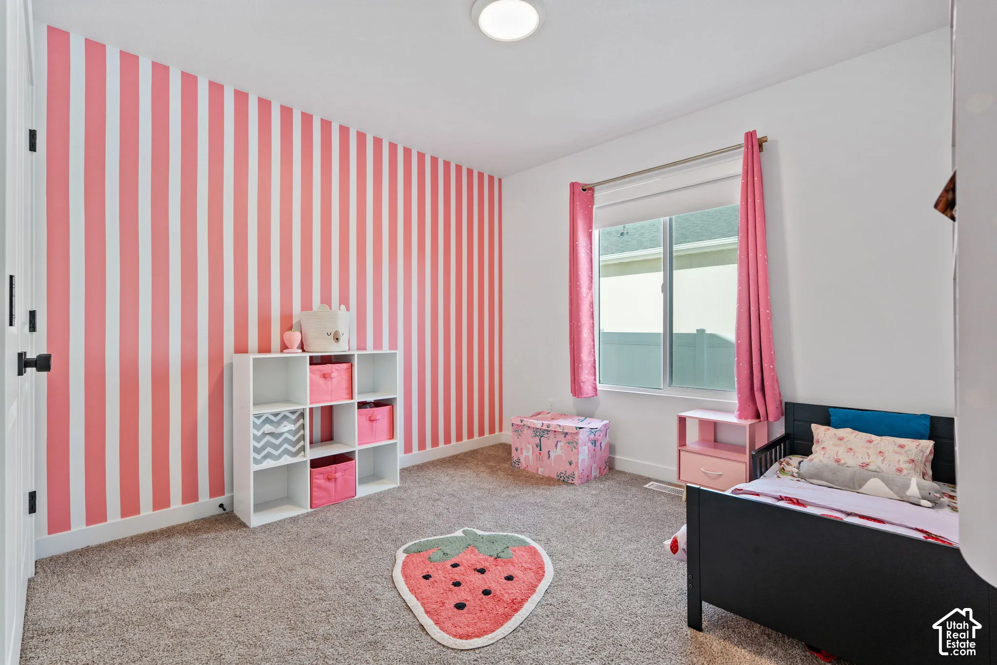 White walls with a bold striped accent wall, light-colored carpeting, a window with a roller shade, and a flush-mount ceiling light fixture