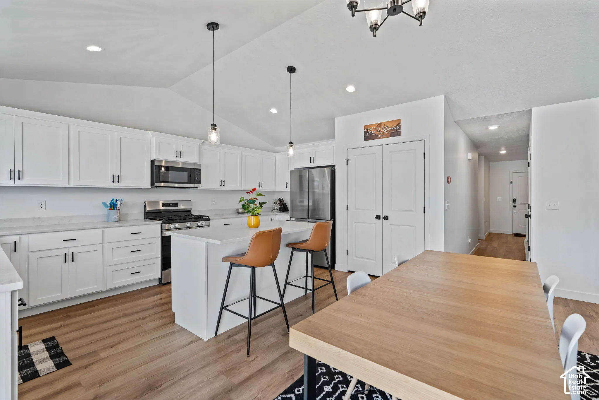 Vaulted ceiling kitchen featuring white cabinetry, stainless steel appliances, a center island, and wood-finish flooring