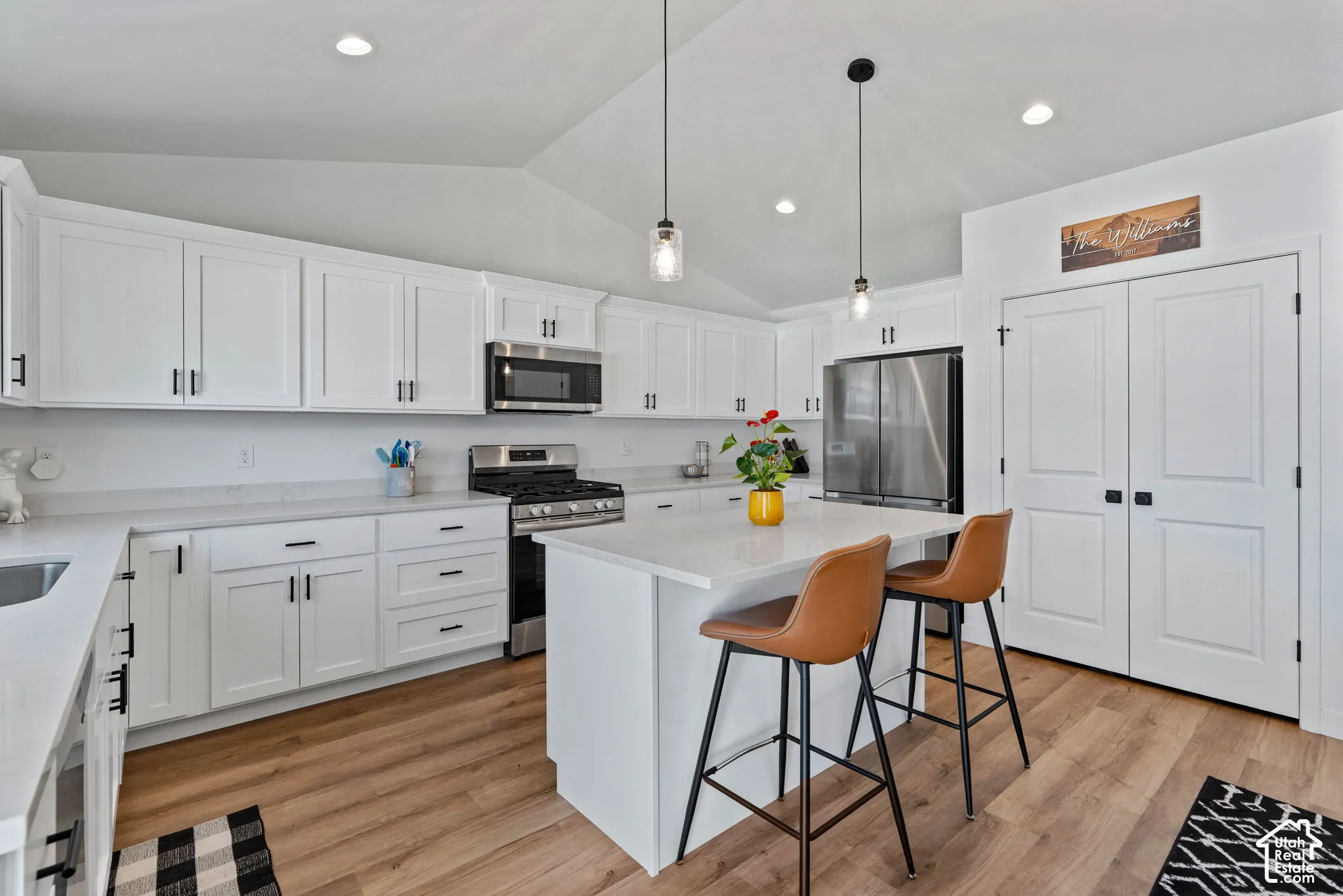 Kitchen featuring wood-finish flooring, white cabinetry, a center island with pendant lighting, and stainless steel appliances