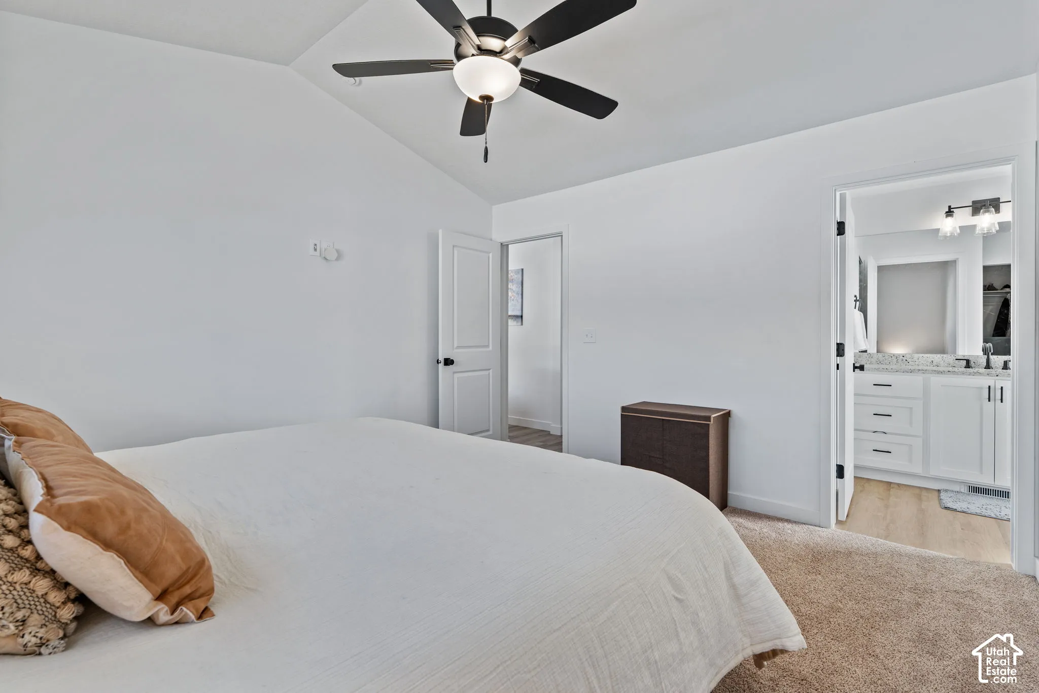 Vaulted ceiling with a ceiling fan, white paneled doors, and a bathroom featuring a vanity with a light-colored countertop