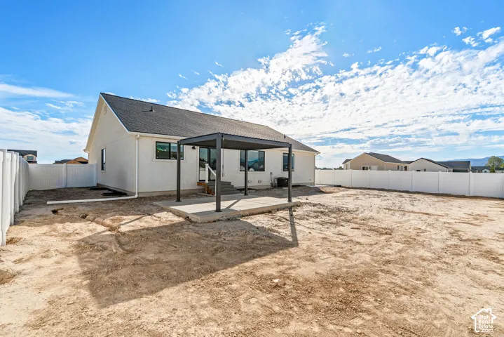 Rear exterior featuring a white vinyl privacy fence, dark gray pergola, concrete patio, and a sloped roofline