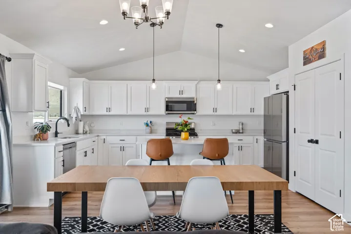 Vaulted ceiling with a contemporary chandelier, white shaker cabinetry, stainless steel appliances, wood-finish flooring, and white countertops