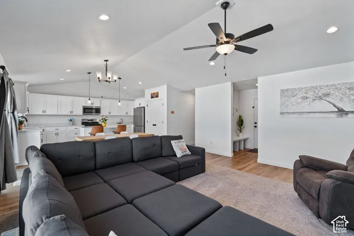 Open-concept living and kitchen area featuring recessed ceiling lighting, a ceiling fan with brushed metal blades, stainless steel appliances, white cabinetry, wood-finish flooring, and a spacious sectional layout with ample natural light from multiple wi