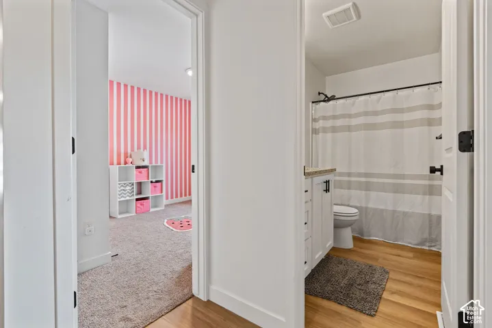 Bathroom featuring wood-finish flooring, a vanity with a light-toned countertop, and a shower with a dark-finish shower rod