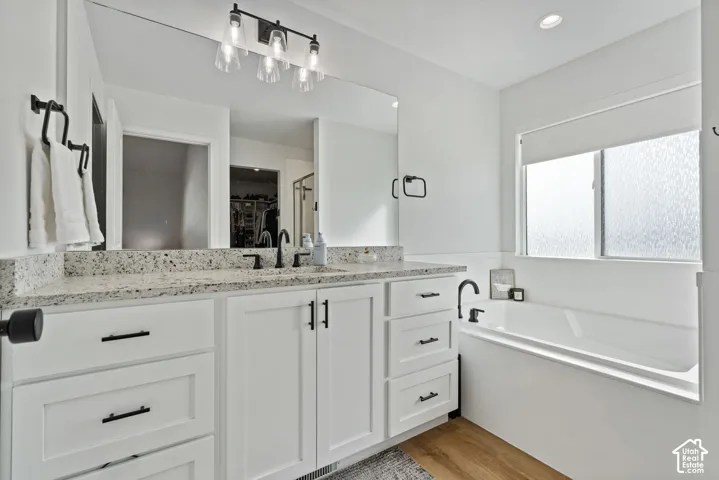 White cabinetry with matte black hardware, dual sinks, speckled countertop, recessed lighting, and a built-in tub