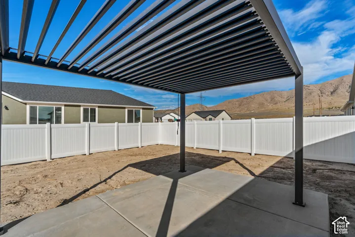Outdoor patio with a louvered pergola, surrounded by white panel fencing