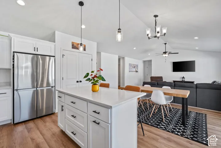 Kitchen featuring a large central island with a solid surface countertop, white cabinetry with dark hardware, stainless steel refrigerator, and wood-finish flooring