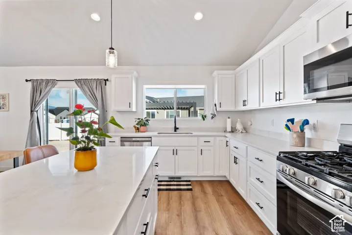 Kitchen featuring white shaker cabinetry, light-toned countertops, wood-finish flooring, stainless steel appliances, and an island with a pendant light