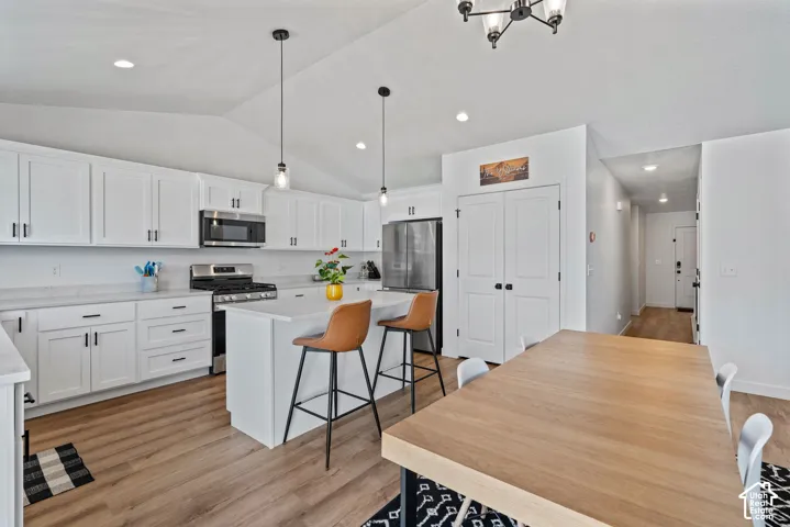Vaulted ceiling kitchen featuring white cabinetry, stainless steel appliances, a center island, and wood-finish flooring