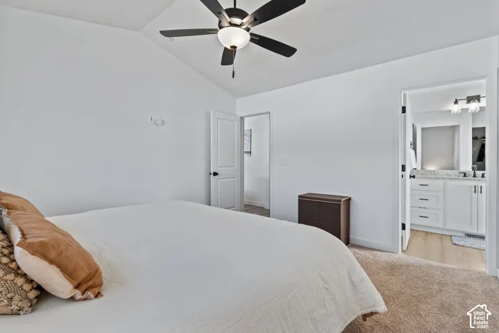 Vaulted ceiling with a ceiling fan, white paneled doors, and a bathroom featuring a vanity with a light-colored countertop