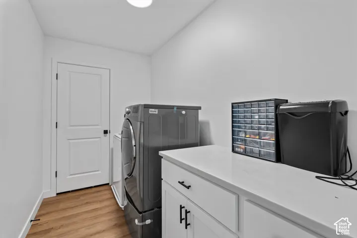 Laundry area featuring wood-finish flooring and white cabinetry with black hardware