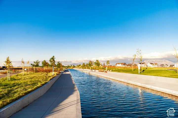 Concrete-lined water feature with an adjacent pathway, surrounded by manicured grassy areas and young trees