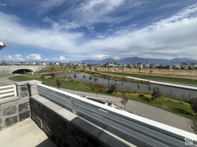 Expansive mountain scenery with a water feature, paved walking paths, and a stone bridge
