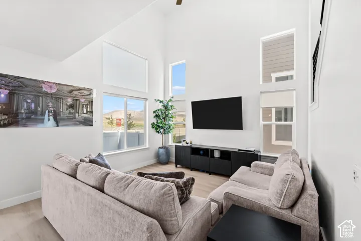 Vaulted ceilings, wood-finish flooring, white walls, multiple windows, and a ceiling fan