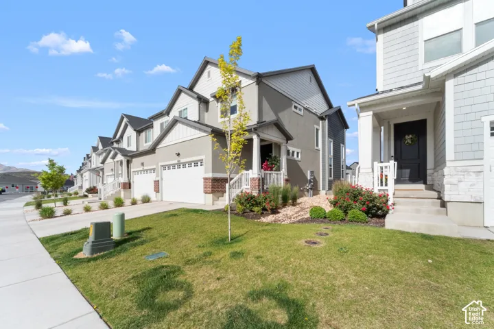 Contemporary townhome featuring a two-car garage, white shaker siding, and a covered front porch with white railing