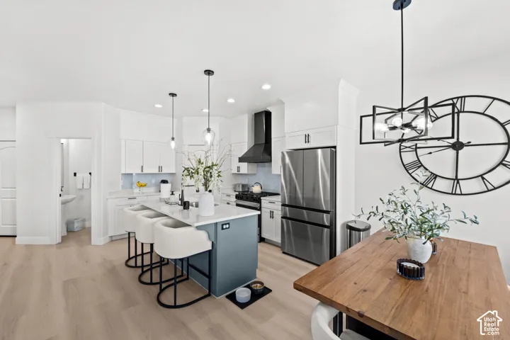 Contemporary kitchen featuring an island with seating, pendant lighting, stainless steel appliances, a range hood, and wood-finish flooring
