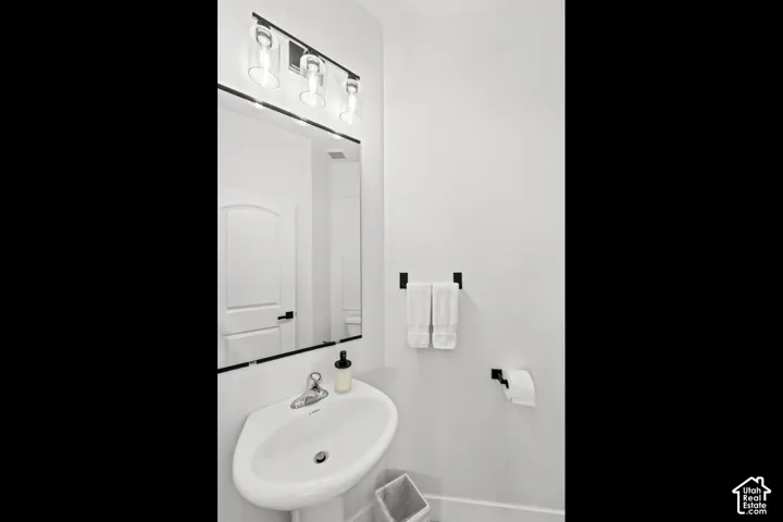 Pedestal sink, wall-mounted mirror, three-light vanity fixture, and black finish hardware