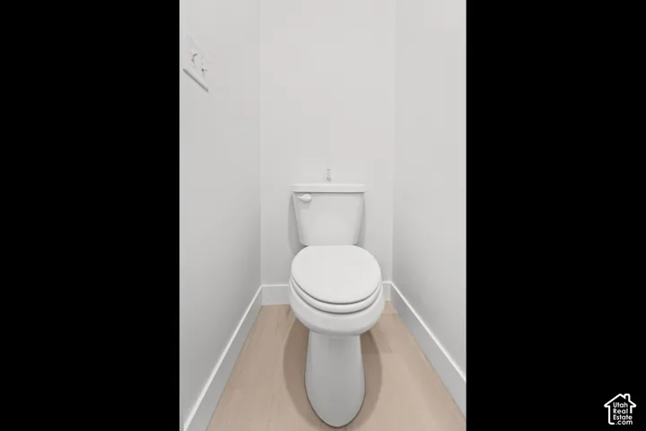 White toilet with a matching tank, set against light-toned walls, featuring wood-finish flooring