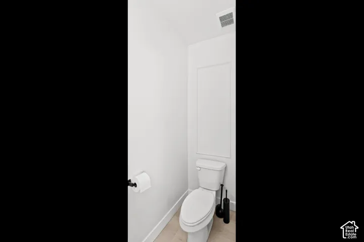 White walls with panel detailing, light wood-finish flooring, and a contemporary toilet